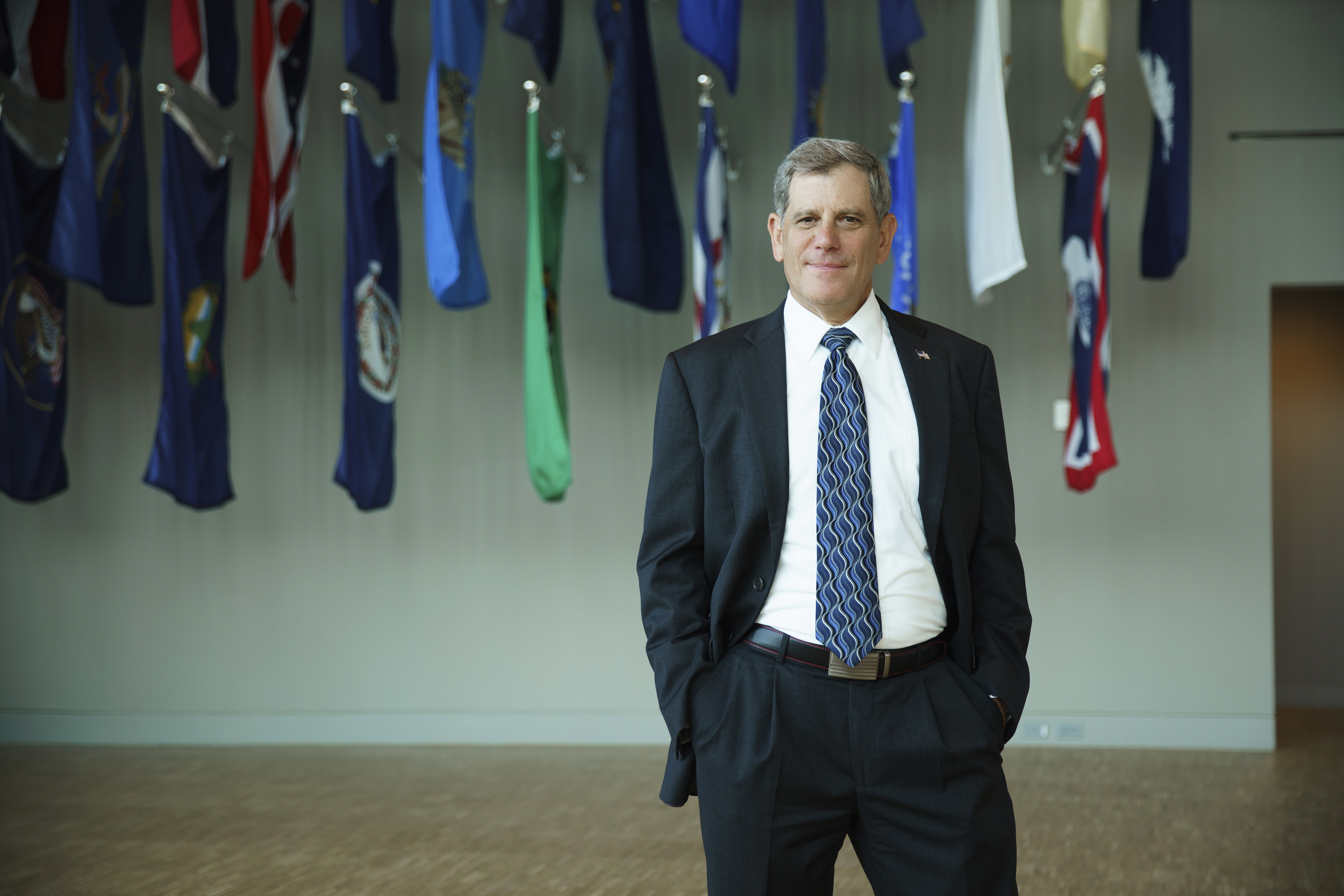 man in suit standing in front of draped flags